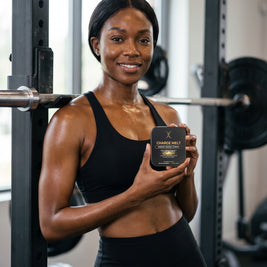 Woman in a black sports bra holding a CHARGE MELT tin beside a squat rack