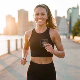 Woman running on a city waterfront path at sunrise with a CHARGE MELT tin