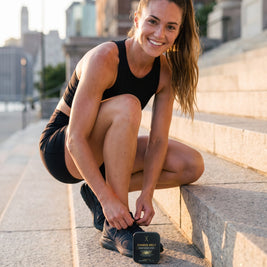 Woman lacing her running shoes on city steps, CHARGE MELT tin beside her shoe