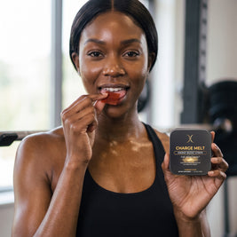 Woman placing a red CHARGE MELT oral strip on her tongue at the gym, tin in hand