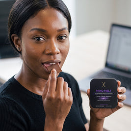 Woman placing a chocolate MIND MELT oral strip on her tongue, tin in hand